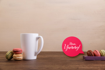 Macaroon cakes. Mockup white tea or coffee cup. Yummy speech bubble. Almond sweet cookies. Wooden rustic board.