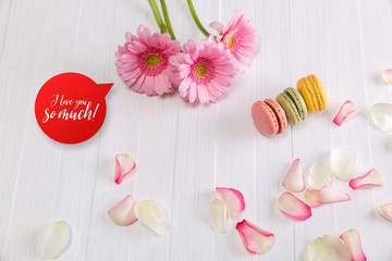 Macaroon cakes with pink rose petals and Gerbera flowers. Different types of macaron. I love you speech bubble. On white wooden rustic background.
