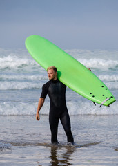 Surfer wearing wetsuit standing on the beach with a surfboard