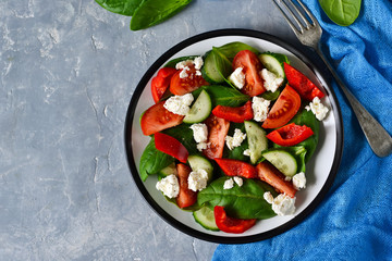 Vegetable salad with tomatoes, spinach and peppers on a concrete, gray background. Top view.