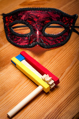 Judaism and religious holiday with wooden noisemaker or gragger (a traditional toy) for purim celebration holiday (jewish holiday) and a red mask on wooden background