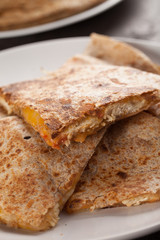 Crispy Quesadilla with Chicken and Sauce on white plate on dark wooden background stacked close up shot