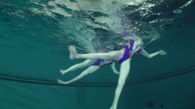 Synchronized swimming, two girls training, underwater view.

