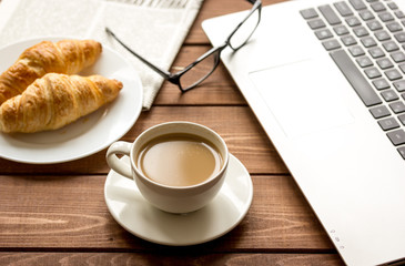 Business lunch with croissant and laptop on wooden desk