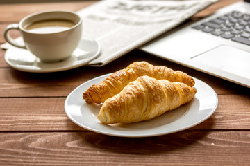 Business lunch with croissant and laptop on wooden desk