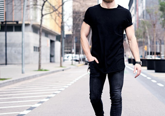 Closeup view of young muscular man wearing black tshirt and jeans walking on the streets of the...