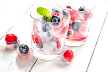 glass with frozen berries in cubes on wooden desk background