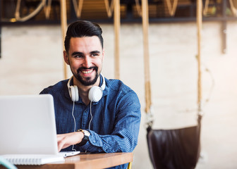 Cheerful Young Man with Beard Working on Laptop in Coffee Shop