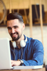 Cheerful Young Man with Beard Working on Laptop in Coffee Shop