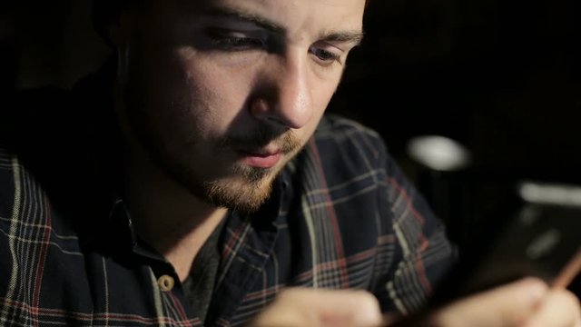 Young man uses the smartphone at night in a restaurant close-up