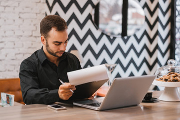 Handsome guy with laptop checking menu at city restaurant