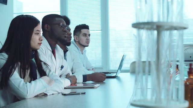 Group of young people students in white coats in chemistry lab listening the lector. Pharmacy classes concept. Footage with copy space