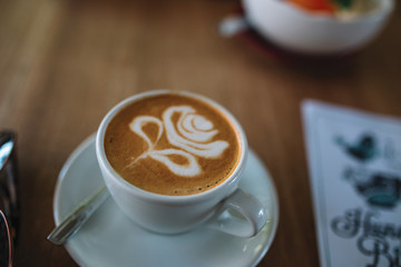 Close up of cup of coffee on the wooden table with a rose