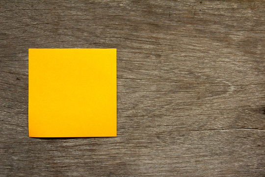 Blank orange note paper attach on brown wooden background for memo or remind
