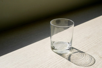 Empty glass shadow on a desk beside a window