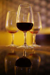One glass of wine and two empty glasses on a table with reflection.