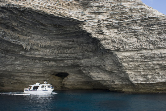 Limestone coastline, with one of the boats that cross to and from the Lavezzi Islands (approximately 10km SE) exiting a cave, Bonifacio, Corsica, France, September 2008