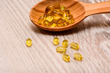 Vitamin D capsules in a wooden spoon on a wooden background, fish oil softgels, health and diet concept 