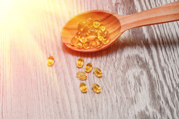 Vitamin D capsules in a wooden spoon on a wooden background, fish oil softgels, health and diet concept with sunshine beams