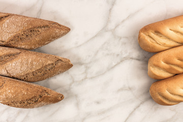 Loaves of rye and wheat bread on a white marble table with a pla