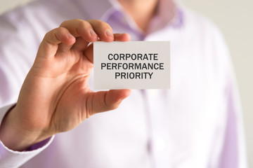 Businessman holding a card with text CORPORATE PERFORMANCE PRIORITY