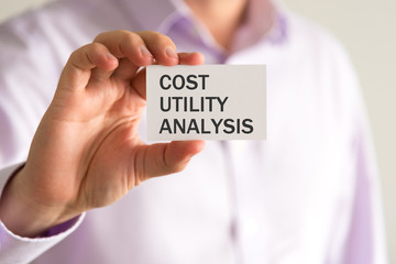Businessman holding a card with text COST UTILITY ANALYSIS