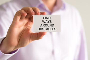 Businessman holding a card with text FIND WAYS AROUND OBSTACLES