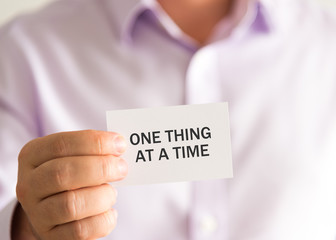 Businessman holding a card with text ONE THING AT A TIME