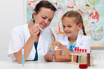 Teacher helping little girl student with elementary chemistry science experiment