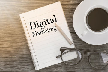 Concept Digital Marketing message on notebook with glasses, pencil and coffee cup on wooden table.