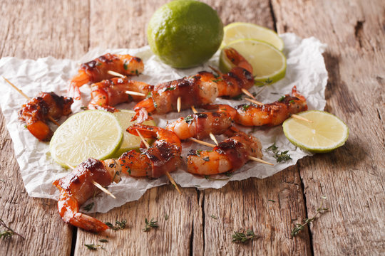 Tiger prawns wrapped in bacon on skewers with thyme and lime close up. Horizontal