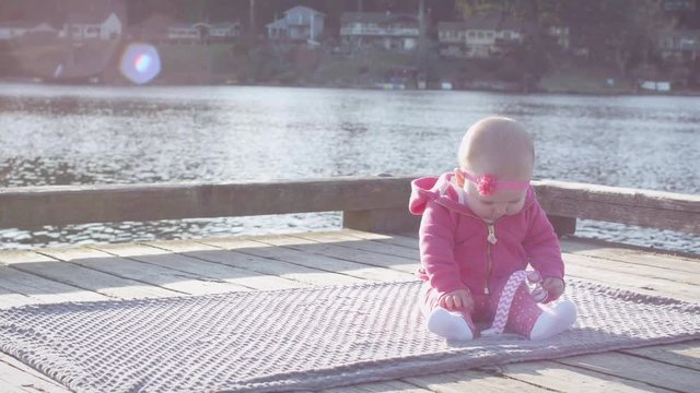 Adorable Baby Girl in Pink Sitting at Lake Dock with Blanket Smiling on Sunny Day Outside