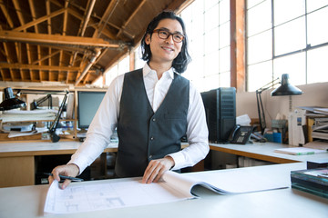 Handsome cheerful male architect at architectural firm office working on project blueprint