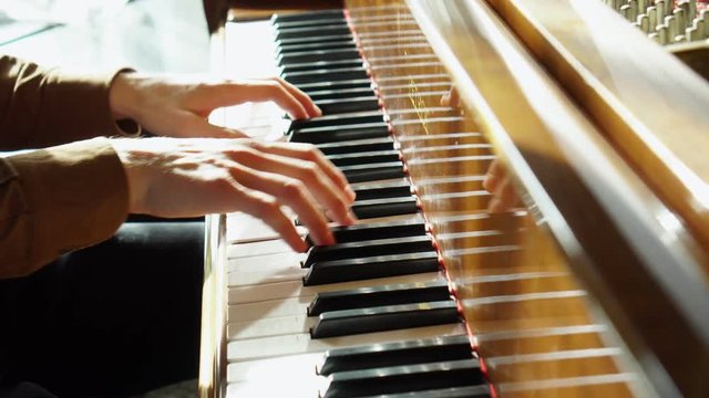 Playing piano. The young man plays a piano. The beautiful pianist plays melodies. Pleasant light from a window indoors. The Pproffesionalny pianist for a piano. Hands it is close to the camera. The