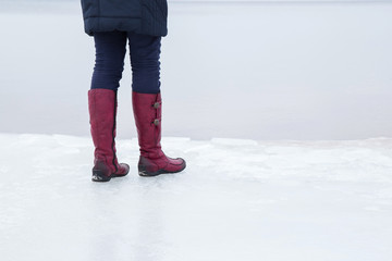Woman walking on the seashore ice surface in winter day. Red winter boots on legs. Active lifestyle at the sea.