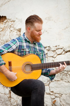 Hipster man with red beard playing a guitar