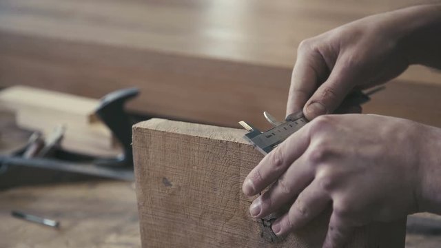Close-up of a calliper in the hands of a joiner or a carpenter. Professional carpenter measures the width of the wood raw bar, using a vernier caliper. Measuring instruments: Scale calipers.