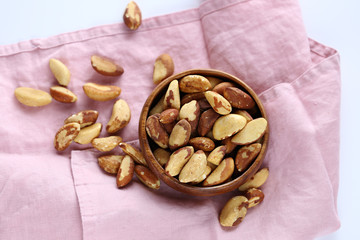 Brazil nuts in a wooden round dish on a pink linen napkin on a white background
