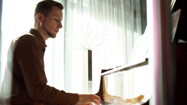 Playing piano. The young man plays a piano. The beautiful pianist plays melodies. Pleasant light from a window indoors. The Pproffesionalny pianist for a piano.