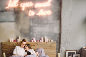 Happy young beautiful caucasian couple lying in bed holding cat. Playing with pet at home. Love, relationships, coziness, leisure, animal protection concept. Tilt-shift image, soft selective focus.