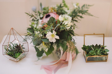 Botanic bridal chic. Bouquet with silk ribbons and florarium with succulents. Tilt-shift image, soft selective focus.