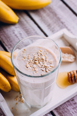 Delicious Healthy breakfast or snack. Banana smoothie with oat flakes, yogurt and honey in glass on wooden table background. Vegetarian food. Top view, copy space