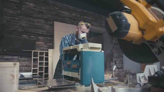 Joiner labouring in mask and glasses for safety. Image of mature carpenter in the workshop. Carpenter cutting wooden board at his workshop. Workplace of cabinetmaker.