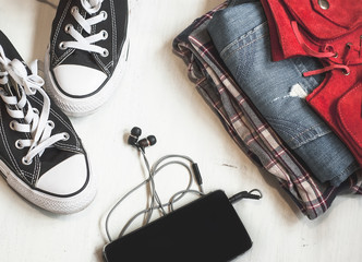 Travel accessories: hipster sneakers, denim shorts, plaid shirt, cowboy belt, hat, sungkasses, map and phone with headphones on wooden background. Selective focus. Traveling concept