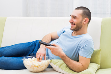 Young man enjoys  watching  tv and eating pop corn.
