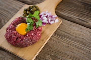Minced meat with egg yolk, onions and olives on wooden tray