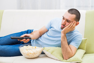 Young man is  feeling boredom and changing channels on tv.