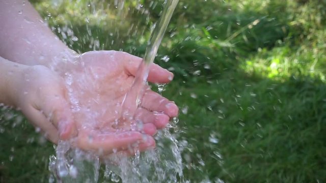 Clean water pouring into woman's hands. Green background. Slow motion