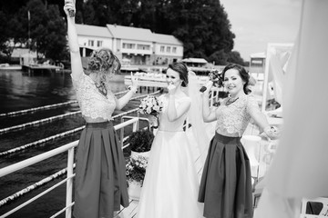 Bride with bridesmaids having fun on pier near lake. Black and white photo.