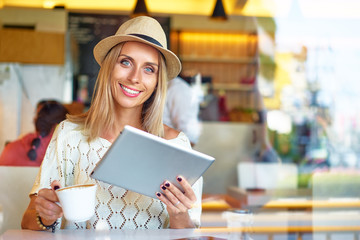 Working at the cafe. Pretty young woman sitting at the table and using tablet computer indoor.